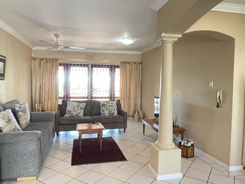 Open plan living area featuring ceramic floor tiles, a decorative column, and an archway leading to the kitchen area.