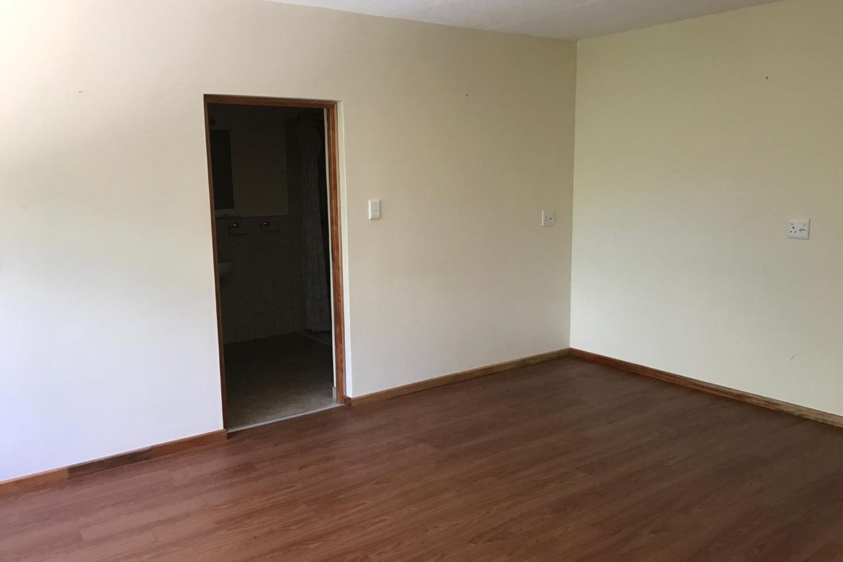 An empty bedroom featuring wood-look laminate flooring and a doorway leading to an adjoining bathroom.