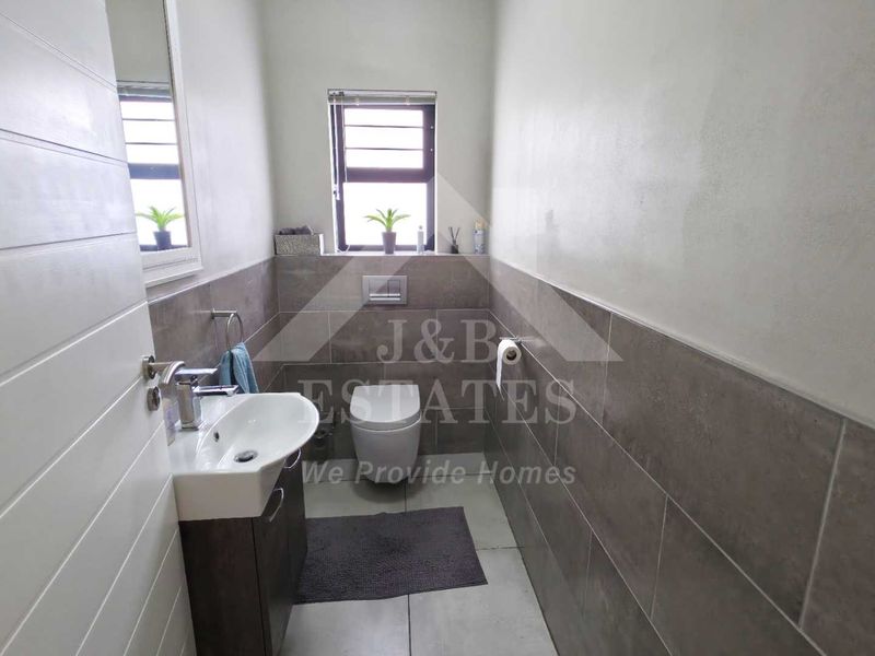 A modern guest bathroom featuring a wall-hung toilet with a concealed cistern, a vanity cabinet with a basin, and neutral tiled finishes.