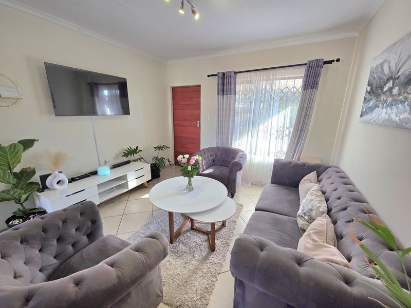 A well-maintained living room featuring tiled flooring, neutral wall finishes, and a security gate leading to the exterior.