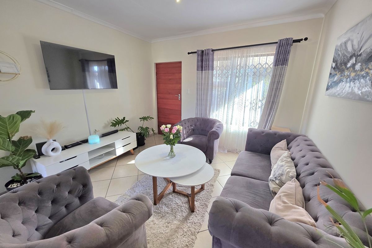 A well-maintained living room featuring tiled flooring, neutral wall finishes, and a security gate leading to the exterior.