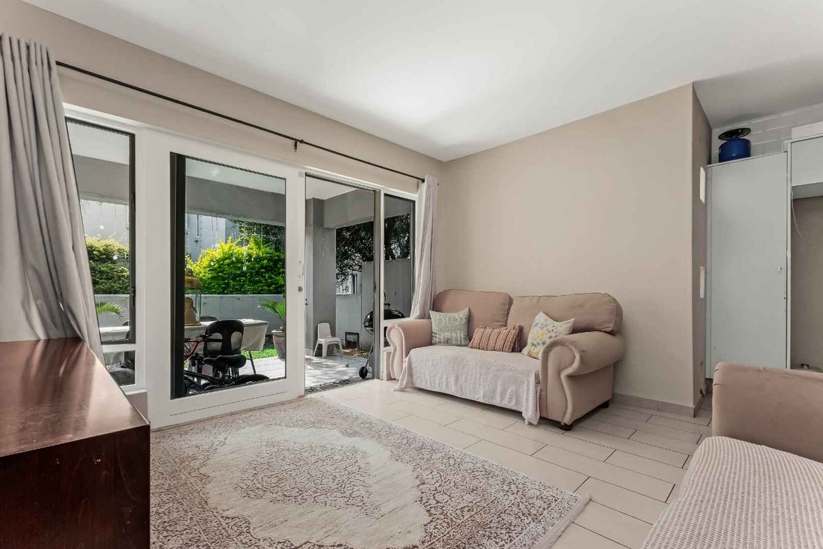 A bright living room featuring large sliding glass doors that open onto a private patio area, with neutral tiled flooring throughout.