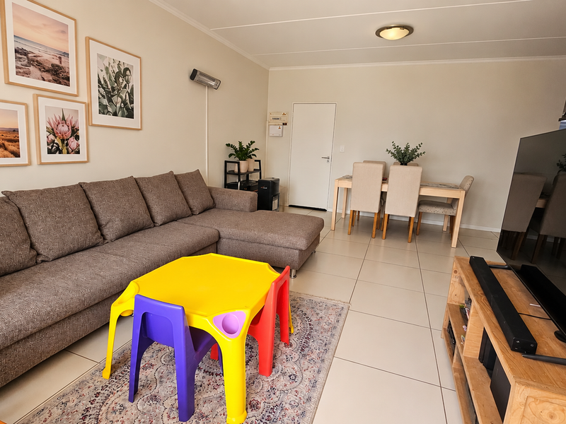 Spacious open-plan living and dining area featuring neutral tiled flooring and a wall-mounted heater, providing a versatile layout for comfortable daily living.