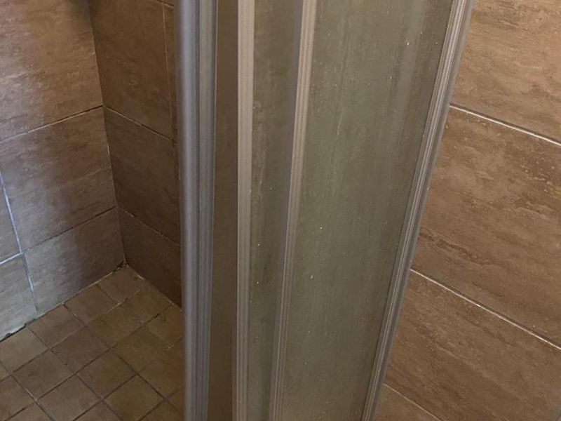 A close-up view of a shower enclosure featuring brown wall tiles and floor tiles, showing signs of wear and aging.
