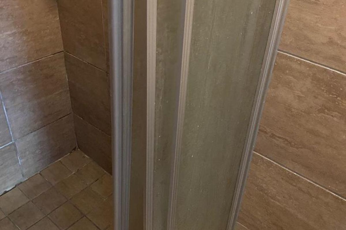 A close-up view of a shower enclosure featuring brown wall tiles and floor tiles, showing signs of wear and aging.
