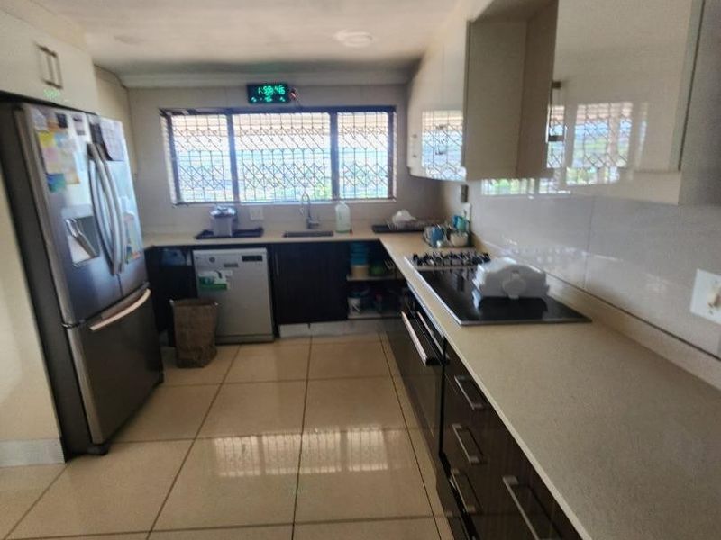 A functional kitchen featuring dark cabinetry, stone countertops, built-in appliances, and tiled flooring, with visible ceiling maintenance required.