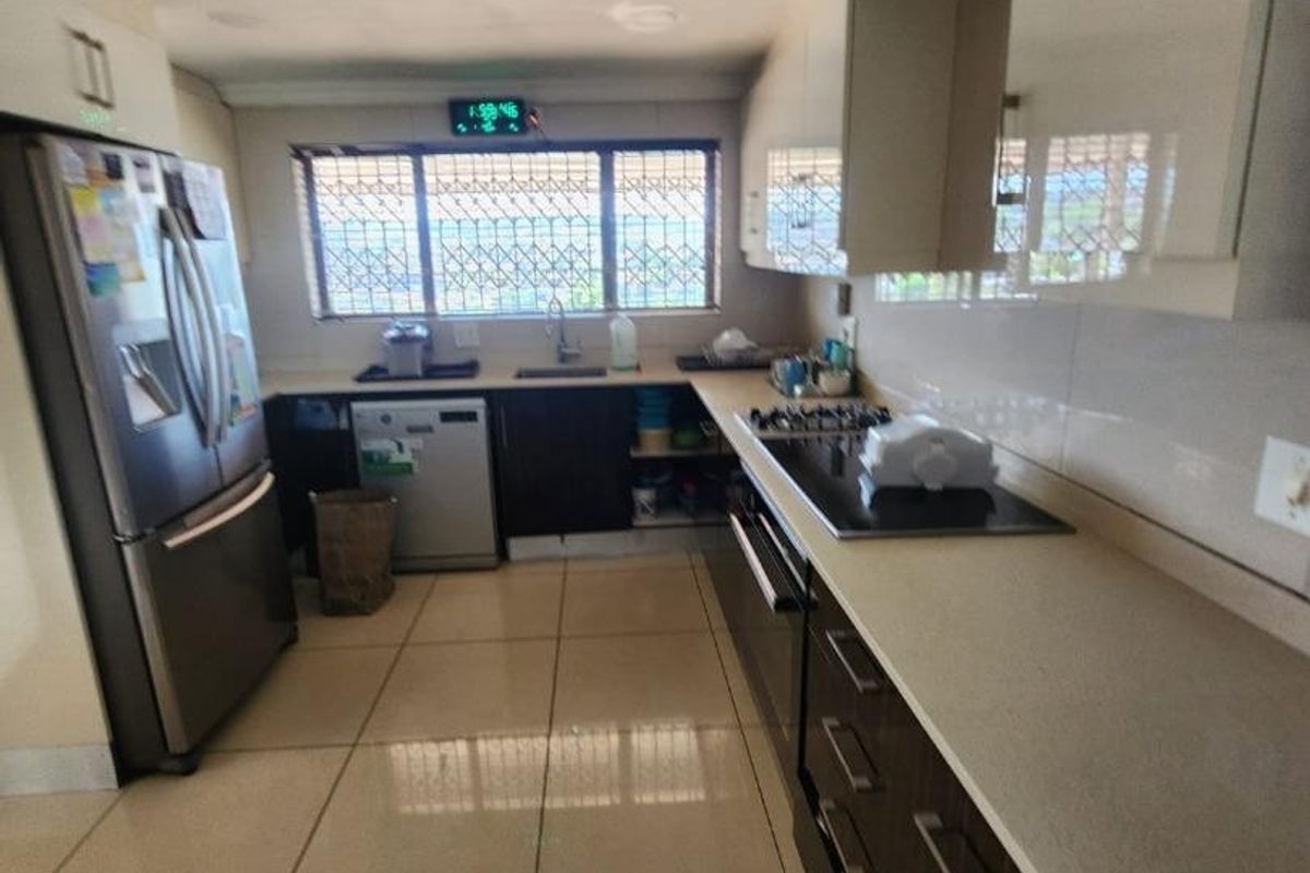 A functional kitchen featuring dark cabinetry, stone countertops, built-in appliances, and tiled flooring, with visible ceiling maintenance required.