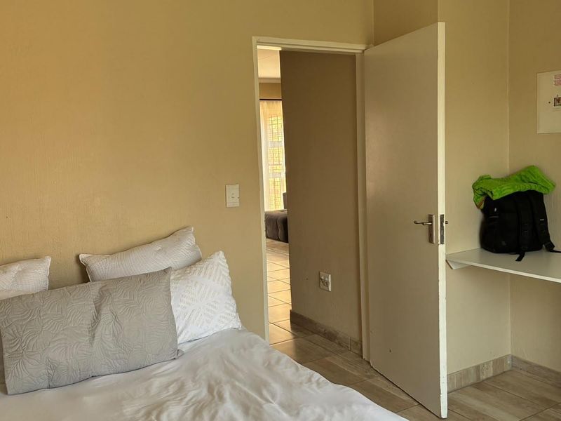 A bedroom featuring tiled flooring, a built-in shelf, and an accessible electrical distribution board, with a doorway leading to an adjacent living space.