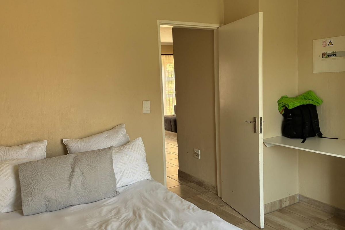 A bedroom featuring tiled flooring, a built-in shelf, and an accessible electrical distribution board, with a doorway leading to an adjacent living space.