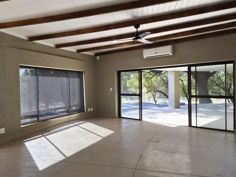 Spacious living area featuring polished concrete floors, exposed timber ceiling beams, and large sliding glass doors opening to an outdoor patio.