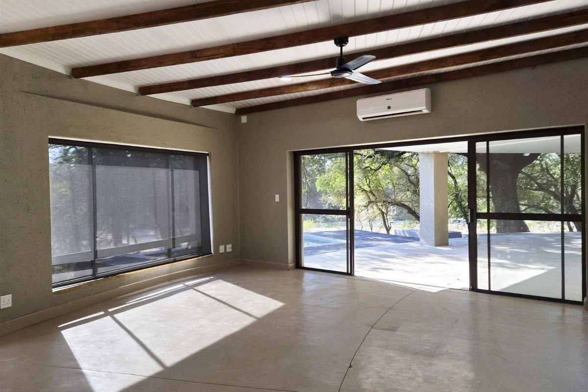 Spacious living area featuring polished concrete floors, exposed timber ceiling beams, and large sliding glass doors opening to an outdoor patio.