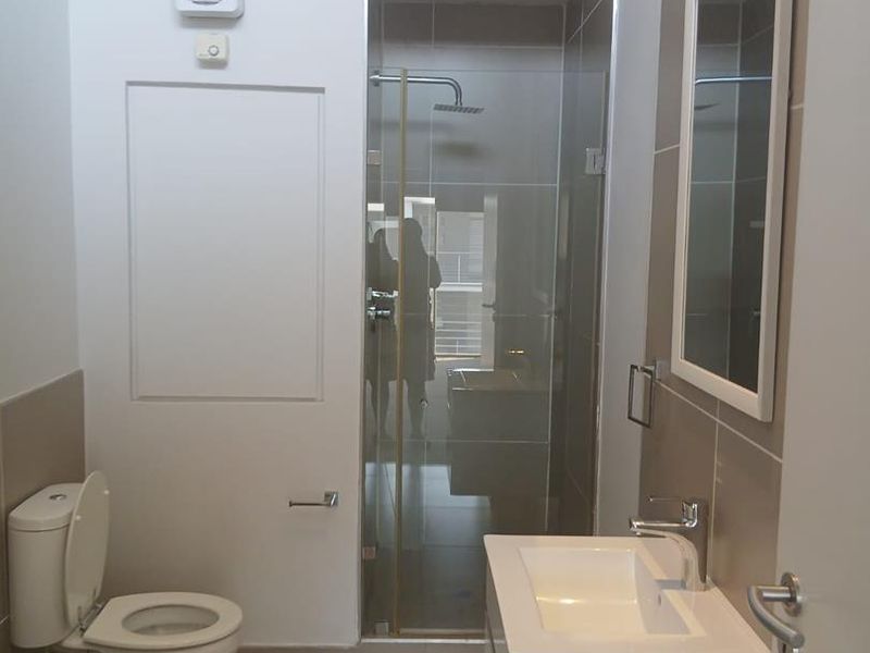 Modern bathroom featuring a glass-enclosed shower, vanity basin with mixer tap, toilet, and neutral tiled finishes.