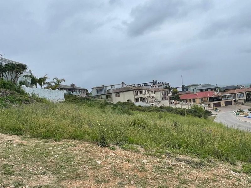 A view of a vacant residential plot with a natural slope, situated in an established neighborhood with surrounding homes.