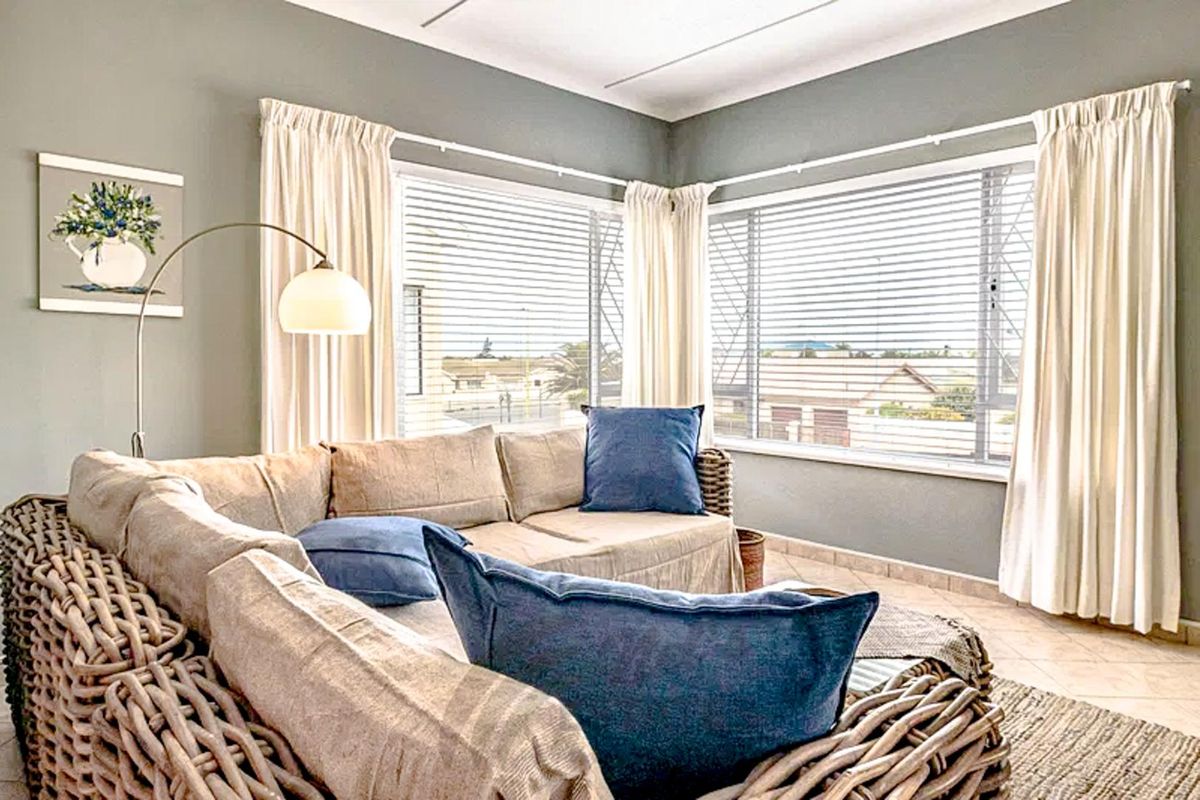 A bright living area featuring large corner windows with fitted blinds, neutral wall tones, and tiled flooring, offering a comfortable and well-lit space.