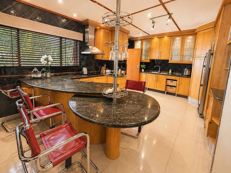 Spacious kitchen featuring extensive wooden cabinetry, granite countertops with integrated breakfast bar, and modern stainless steel extractor fan.