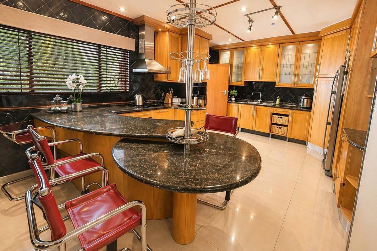 Spacious kitchen featuring extensive wooden cabinetry, granite countertops with integrated breakfast bar, and modern stainless steel extractor fan.