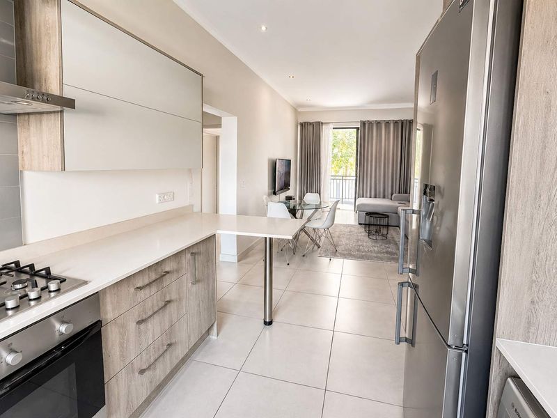 Modern open-plan kitchen and living area featuring sleek cabinetry, stone countertops, integrated appliances, and large sliding doors leading to a private balcony.