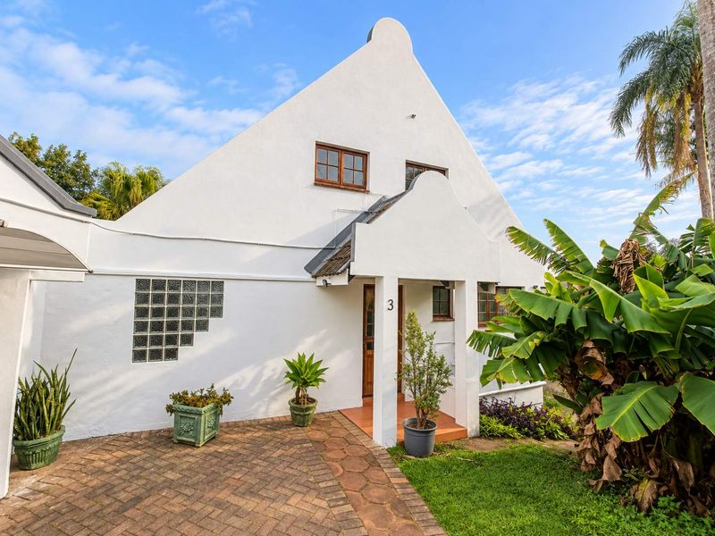 A charming Cape Dutch style home featuring a distinctive gabled facade, glass block detailing, and a welcoming covered entrance porch with brick paving.
