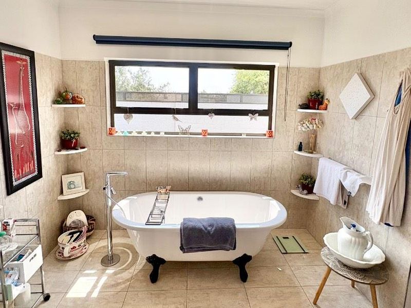 A well-maintained bathroom featuring a modern freestanding bathtub with floor-mounted mixer, neutral tiled finishes, and built-in corner shelving under a large window.