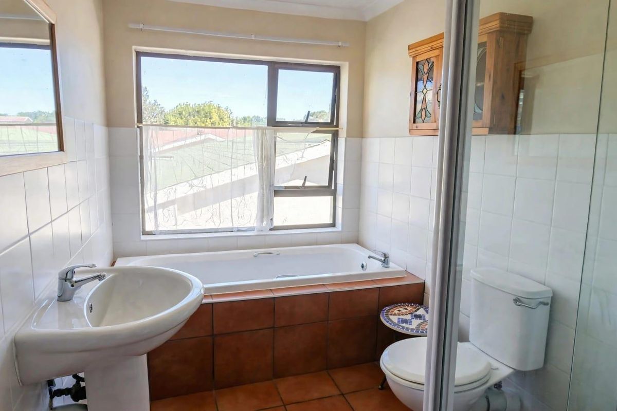 A functional bathroom featuring a pedestal basin, built-in bathtub with tiled surround, separate shower enclosure, and a wall-mounted storage cabinet.