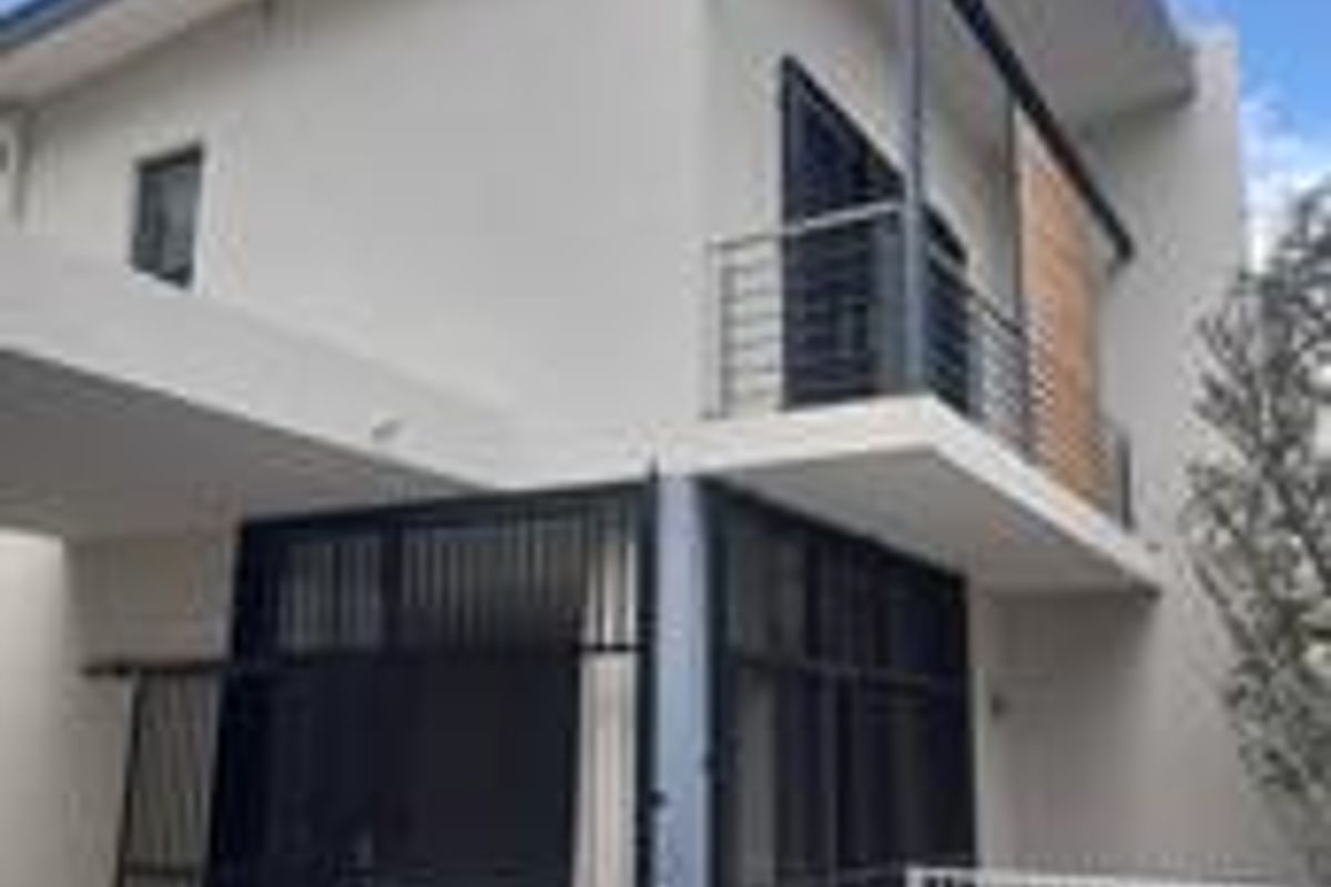 Modern townhouse exterior featuring a private swimming pool, upper-level balcony with metal railing, and contemporary architectural design with large glass sliding doors.