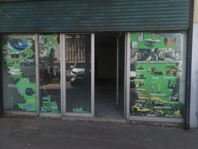 Commercial storefront entrance featuring a metal roller shutter and large glass display windows with existing business branding.