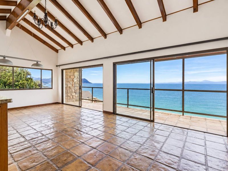Spacious living area featuring exposed timber beams, terracotta flooring, and expansive sliding glass doors opening to a balcony with panoramic ocean views.