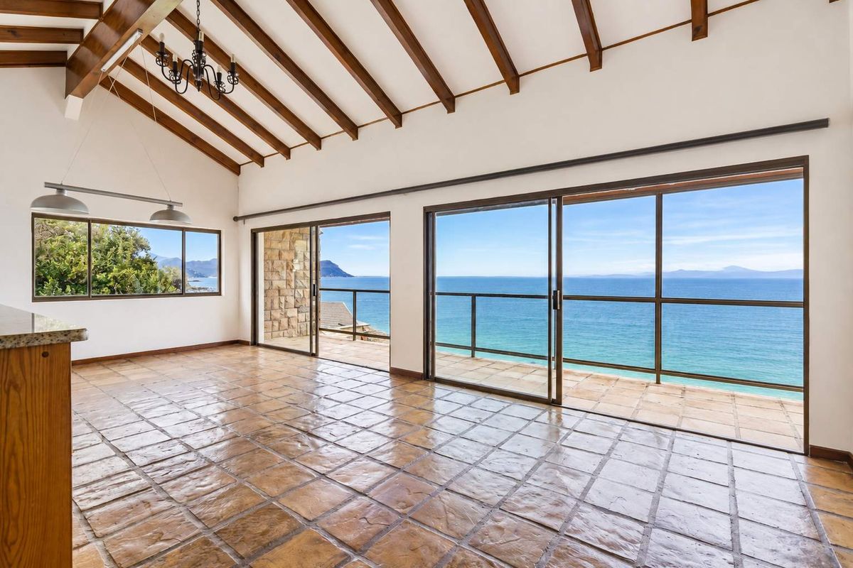 Spacious living area featuring exposed timber beams, terracotta flooring, and expansive sliding glass doors opening to a balcony with panoramic ocean views.