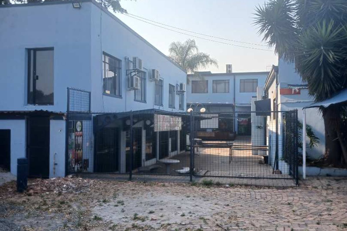 Exterior view of a mixed-use property featuring a paved courtyard area, metal security fencing, and multi-level building structures with visible wear.