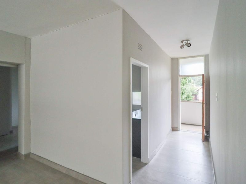 A bright, empty hallway featuring neutral tiled flooring and direct access to an outdoor balcony area.