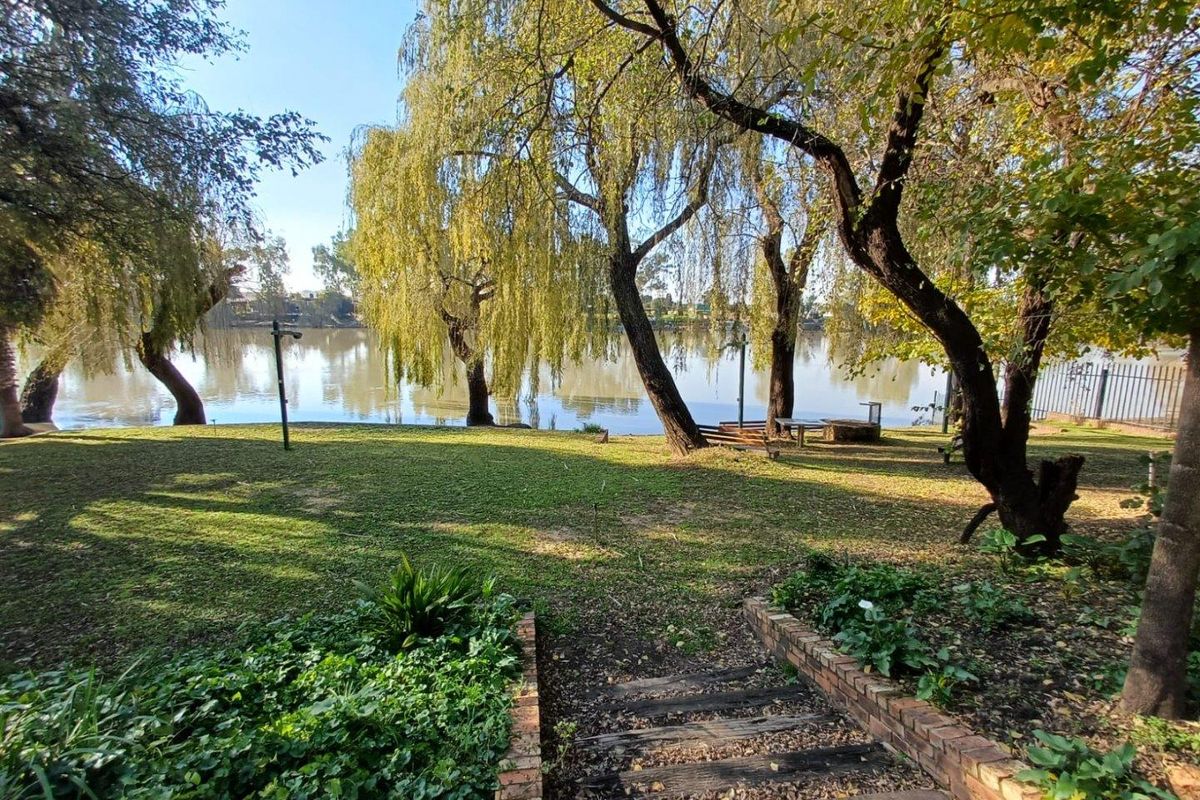 A scenic garden area featuring mature willow trees, brick-edged steps, and direct access to a tranquil riverfront setting.