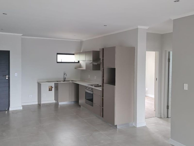 Modern open-plan kitchen featuring sleek built-in cabinetry, integrated oven and hob, and neutral tiled flooring in a bright, spacious apartment setting.