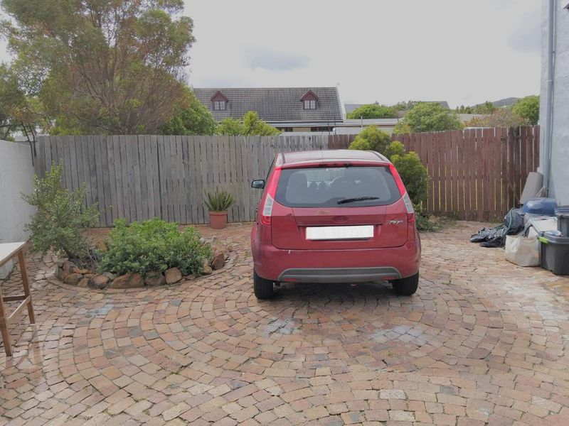 A rear outdoor area featuring a circular paved driveway, timber perimeter fencing, and established garden beds.