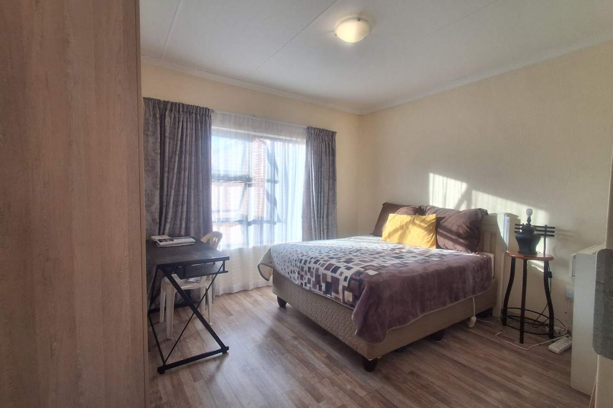 A functional bedroom featuring laminate flooring, a built-in cupboard, and natural light through a window with curtains.