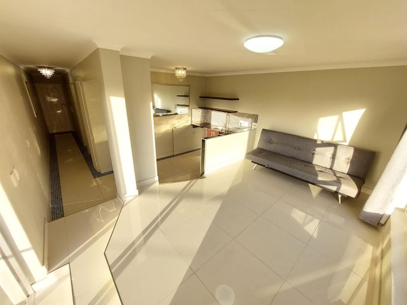 Open plan living area featuring tiled flooring, a compact kitchen with mosaic backsplash, and neutral finishes throughout.