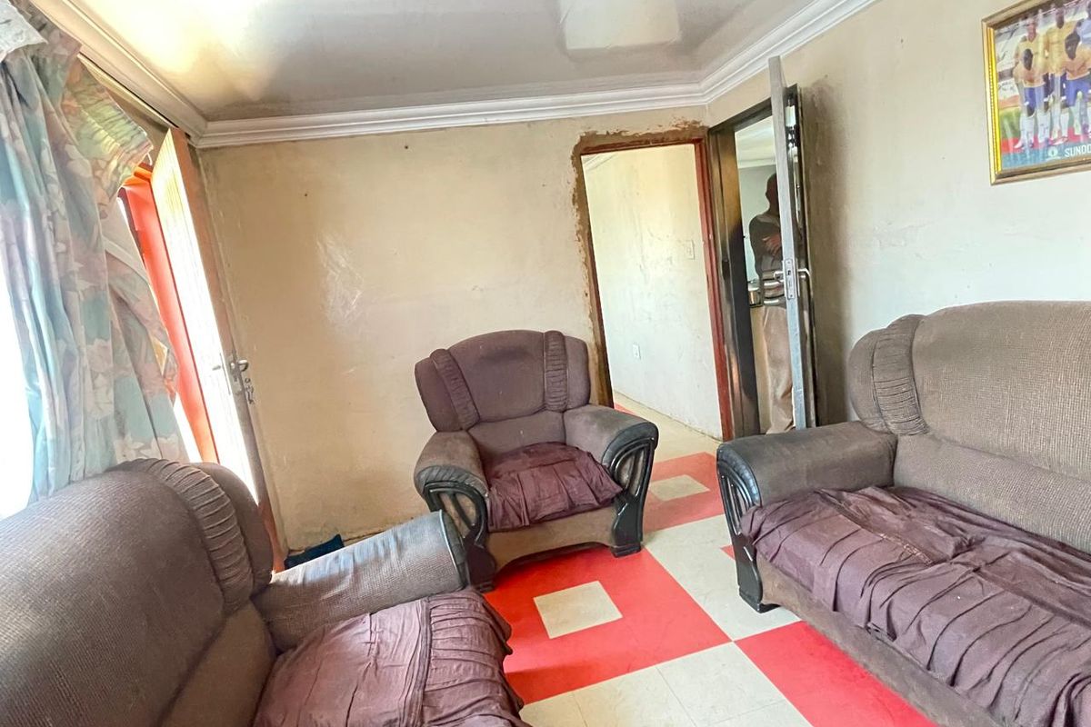 A living room area featuring tiled flooring and plain walls, requiring cosmetic updates and repairs to the wall finishes and door frames.