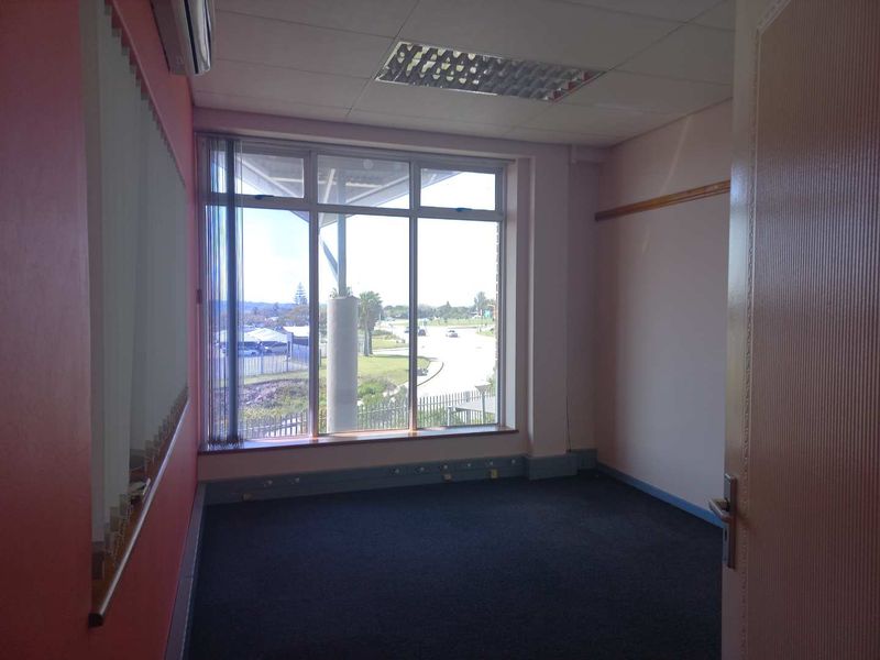 An empty office space featuring large windows with natural light, recessed ceiling lighting, air conditioning, and dark carpeting.