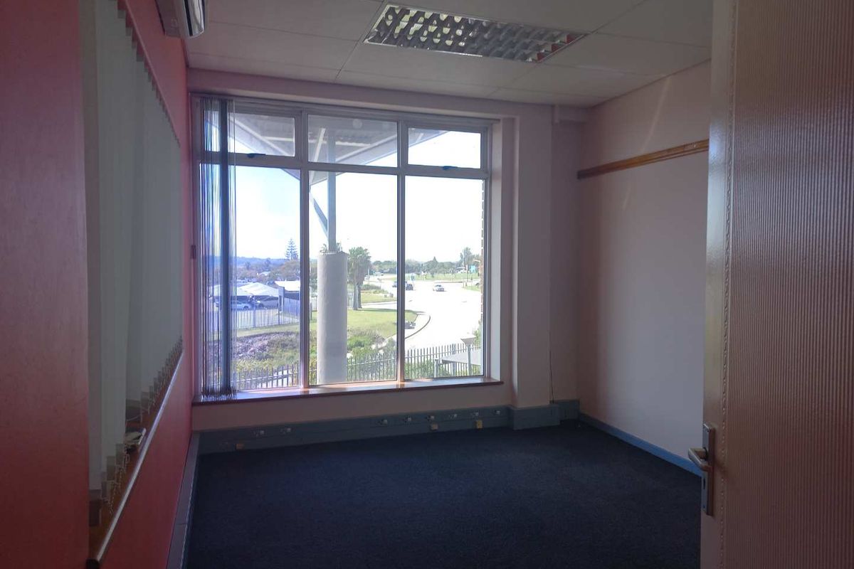 An empty office space featuring large windows with natural light, recessed ceiling lighting, air conditioning, and dark carpeting.