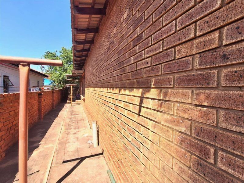 A side exterior view of the property featuring a face brick wall, paved walkway, and a brick boundary wall.