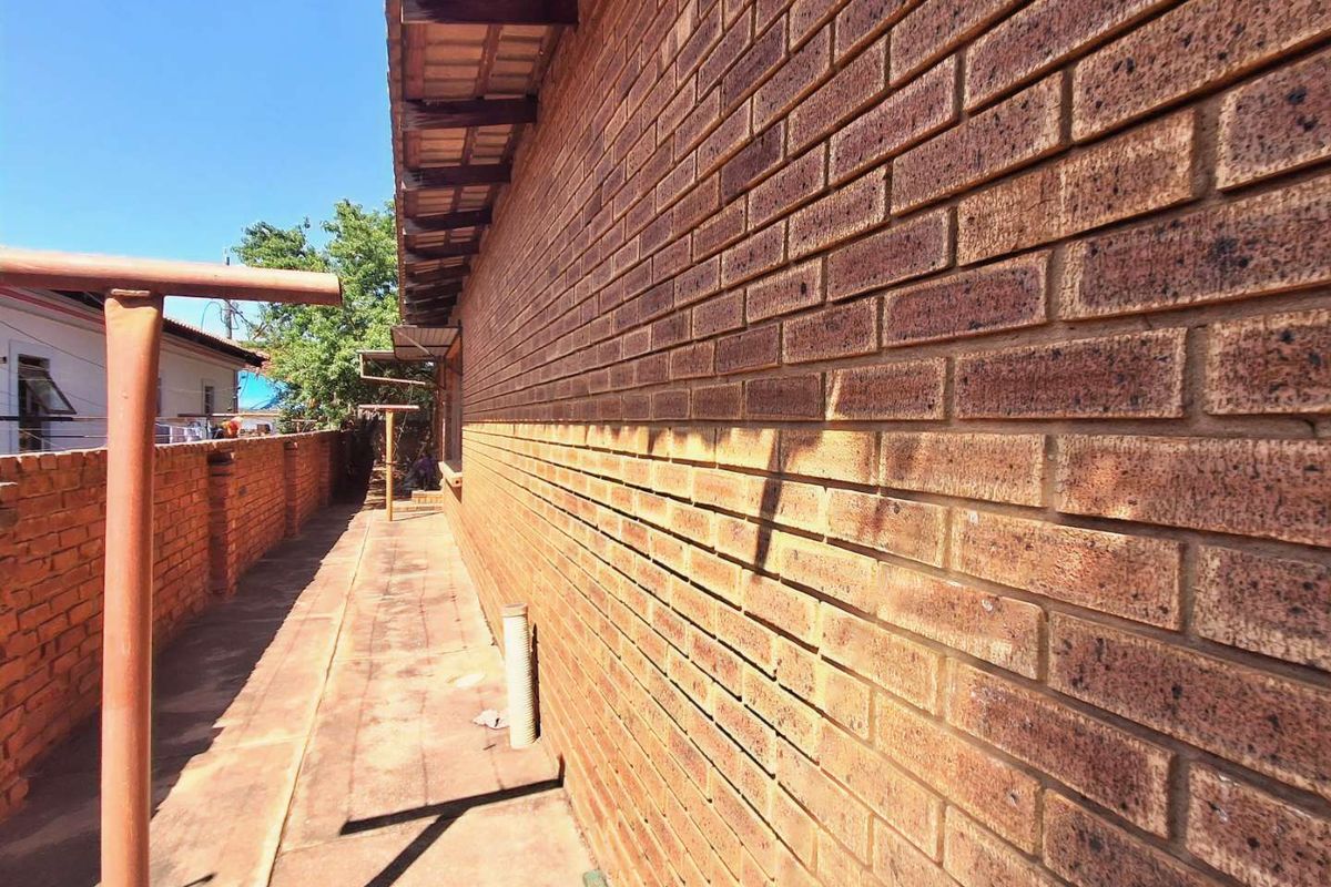 A side exterior view of the property featuring a face brick wall, paved walkway, and a brick boundary wall.