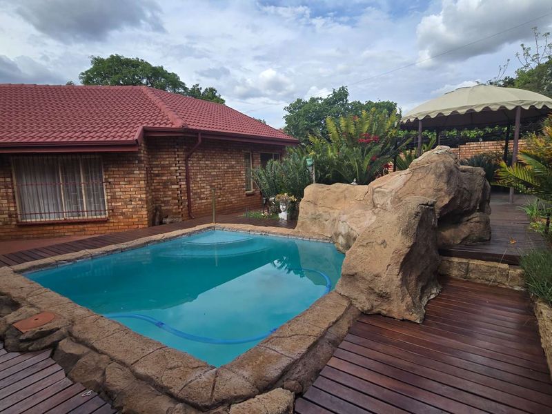Outdoor pool area featuring a rock-scaped swimming pool, timber decking, and a gazebo, set against a brick house with a tiled roof.