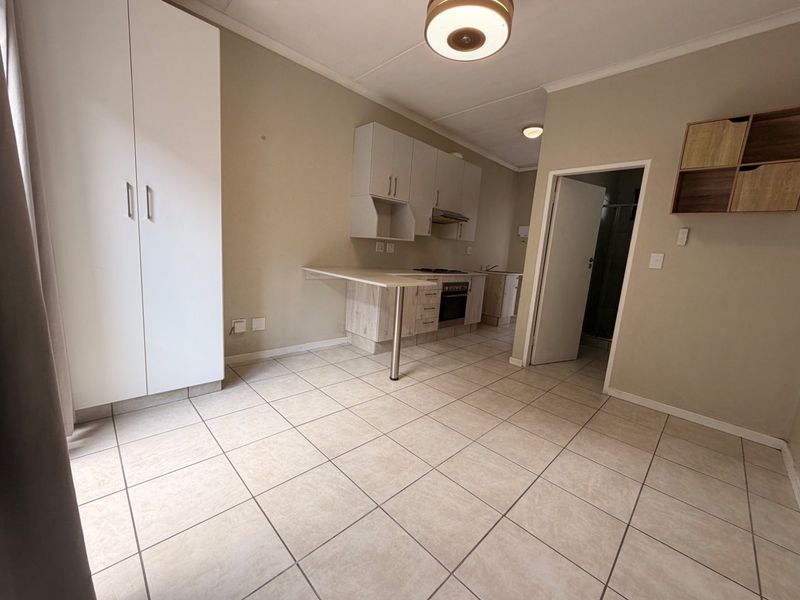 Open-plan kitchen and living area featuring tiled flooring, built-in cabinetry, an integrated oven, and a breakfast counter, offering a functional and versatile living space.