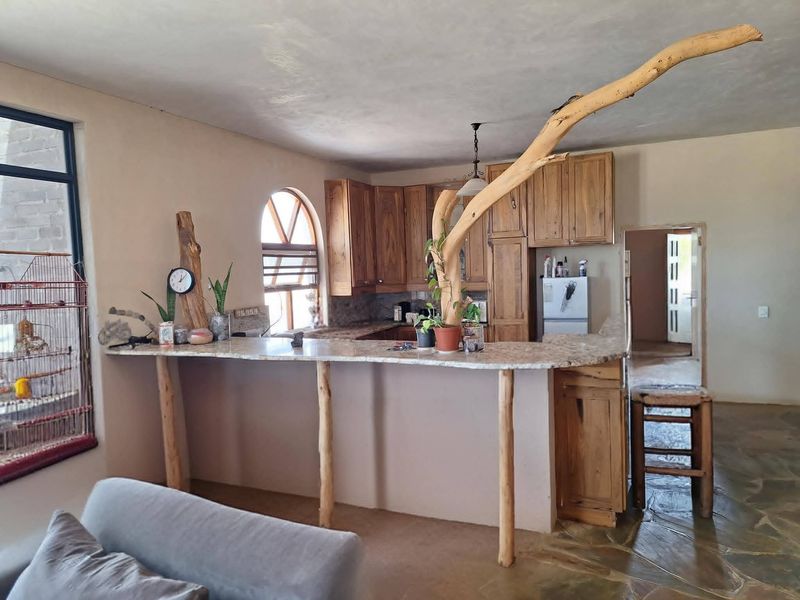 Open plan kitchen area featuring rustic wooden cabinetry, a granite breakfast bar with natural wood supports, and unique arched window detailing.