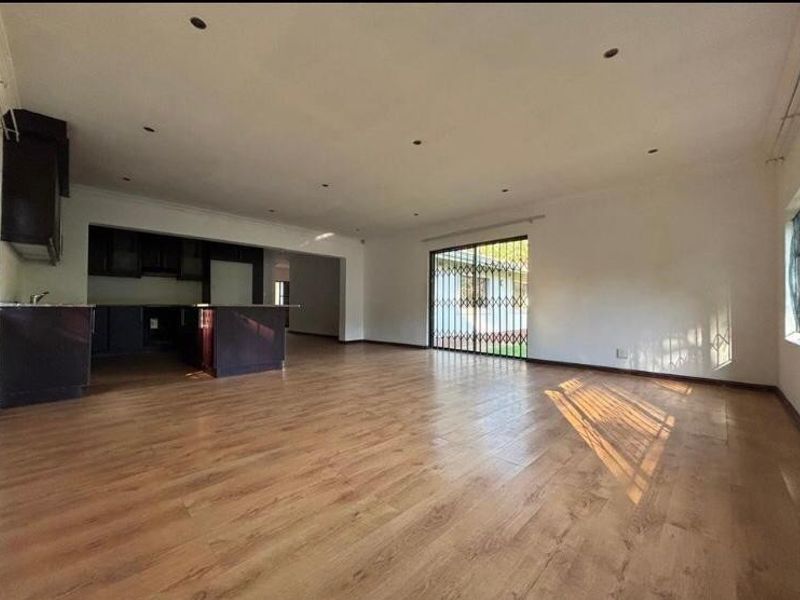 Spacious open-plan living area featuring laminate flooring, recessed lighting, and a functional kitchen layout with direct access to the exterior through a security gate.