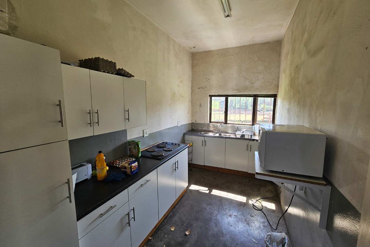 A functional kitchen space featuring built-in cabinetry, an electric hob, and a double sink, requiring cosmetic updates to the walls and flooring.
