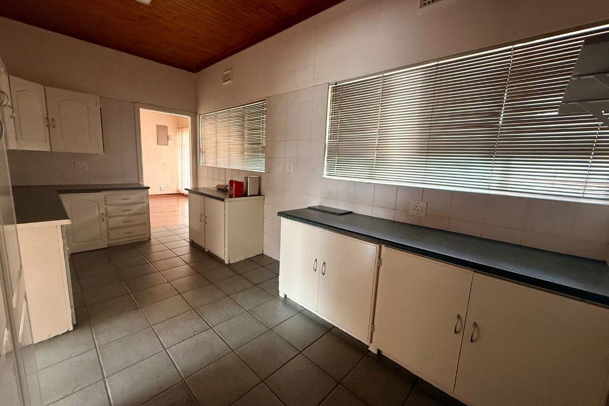 A spacious, functional kitchen featuring tiled flooring, timber ceiling, and ample cabinetry with laminate countertops, offering significant potential for modern renovation.