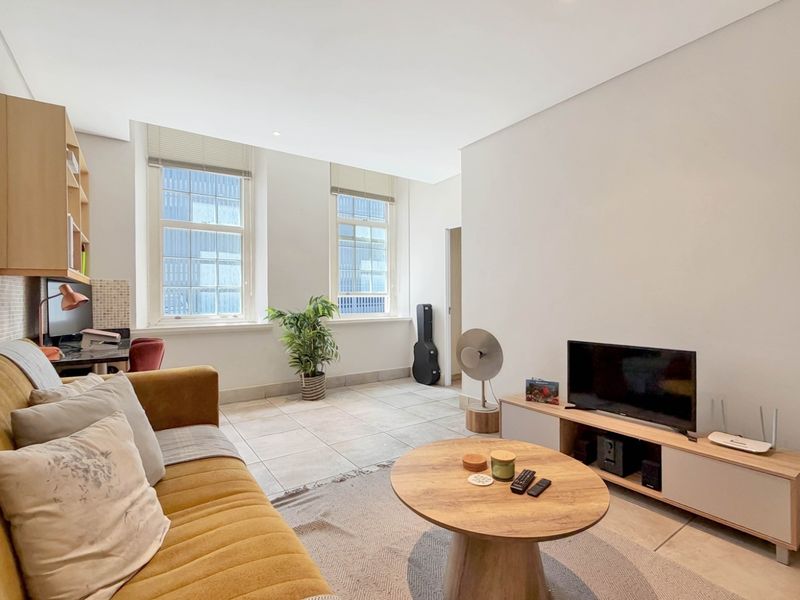A bright and airy living room featuring large sash windows, neutral tiled flooring, and built-in shelving, offering a comfortable and well-lit living space.