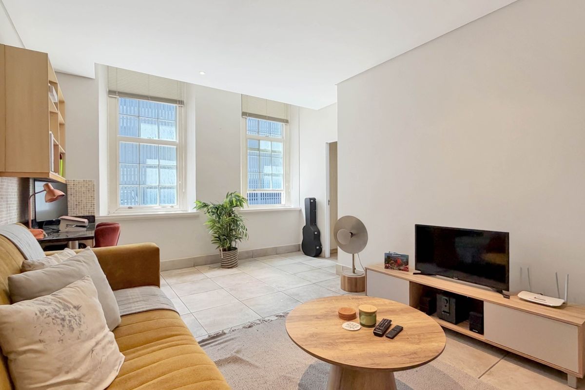 A bright and airy living room featuring large sash windows, neutral tiled flooring, and built-in shelving, offering a comfortable and well-lit living space.