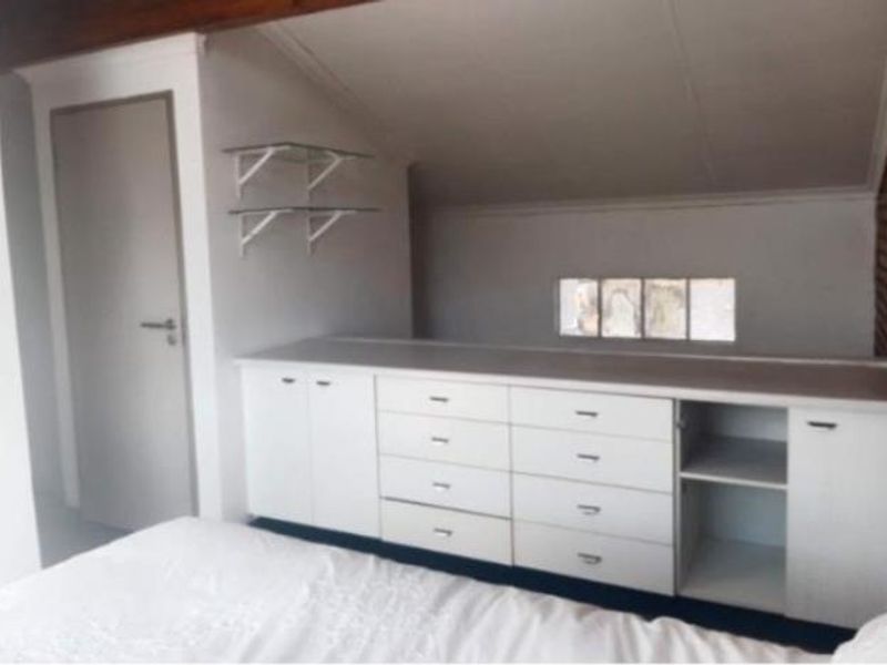 Bedroom featuring built-in white cabinetry, sloped ceilings, and glass shelving, offering practical storage solutions within a compact attic-style space.