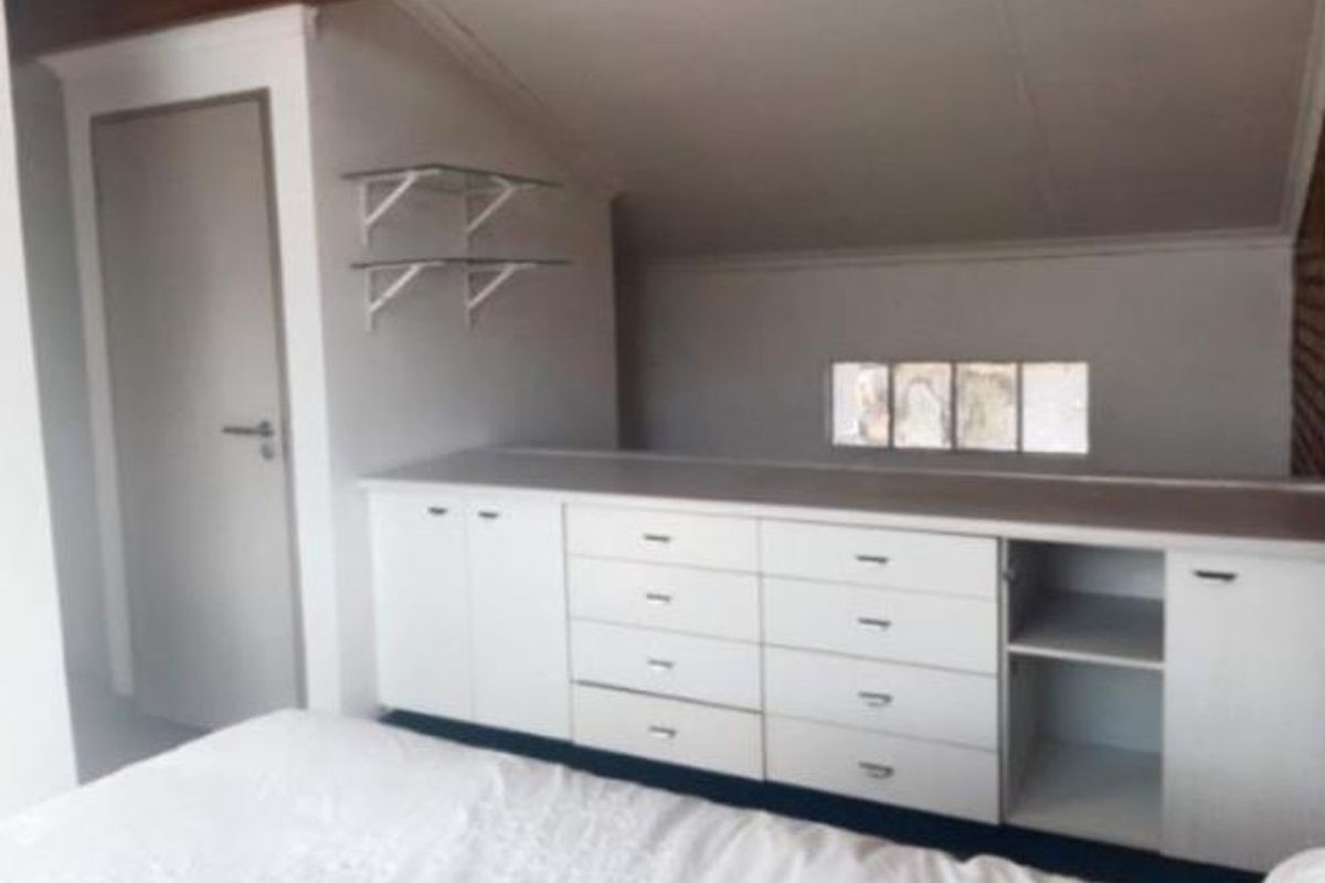 Bedroom featuring built-in white cabinetry, sloped ceilings, and glass shelving, offering practical storage solutions within a compact attic-style space.